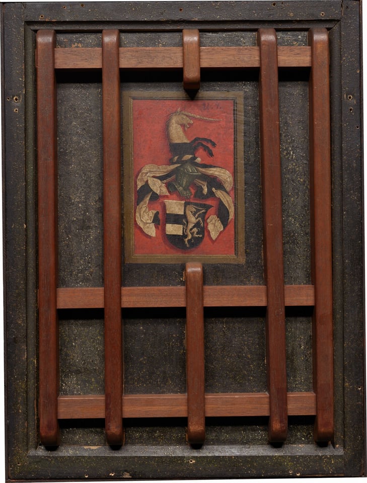 This is a painting depicting a heraldic coat of arms. The image features a detailed coat of arms with a central shield, adorned with black and gold sections, and additional decorative elements above it. There is a figure resembling a unicorn emerging from the crest. The background is a deep red hue. The artwork is displayed within a wooden frame with crossbars. This style is associated with displaying family crests and lineage.