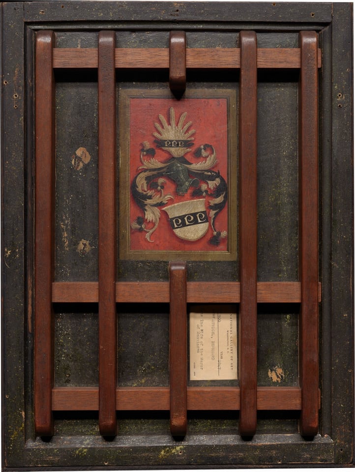 The image shows a pattern of vertical and horizontal wooden bars forming a grid-like design. In the center, there is a rectangular panel with a decorative emblem against a red background. The emblem features swirling shapes. The structured wooden grid and ornate emblem suggest a vintage heraldic shield or coat of arms.