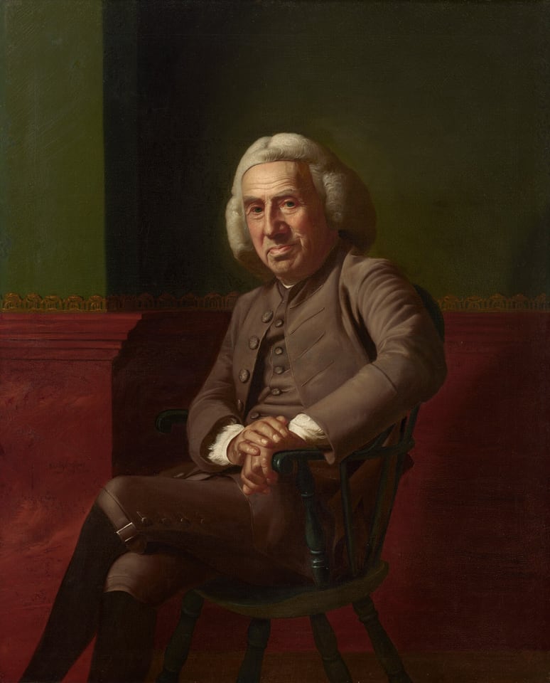 A pale-skinned, clean-shaven man with a heavily lined, paunchy face sits against a green and red wall in this vertical portrait painting. The man sits in a wooden chair painted forest green and rests both hands on the closer arm. His body and knees are angled to our left, and he turns his wide, square face to look at with heavy-lidded eyes. One brow seems slightly cocked, and he has a large nose. His lips are pulled up on one side over a round double chin. He wears a white, shoulder-length wig and a sable-brown suit. The cuffs of a white shirt are visible at his wrists where his hands are stacked on the arm of the chair. The knee-length breeches are buckled at the knee over black stockings. His legs are crossed away from us, and his feet extend off the bottom edge of the composition. The bottom half of the wall behind him is painted burgundy red up to and including a chair rail, and the wall above is moss green. The wall is lined with a gold scallop pattern along the top of the chair rail and a sliver of brown on across the bottom of the composition suggests a wood floor. The artist signed and dated the painting as if he had inscribed the red wall near the man’s knees, “John Singleton Copley pinx 1772. Boston.”