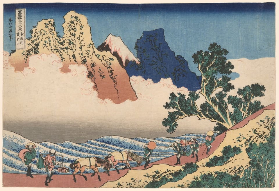Print showing a string of travelers with horses walking along a narrow hillside path beneath an enormous craggy beige mountain at left and an equally massive and craggy deep-blue mountain at right. A brown snow-covered peak appears between these mountains. A mass of cream-colored clouds and a river with rounded ripples fill the middle plane of the composition.