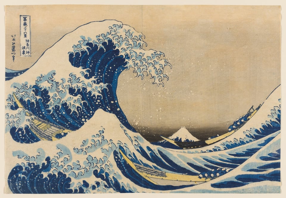 A color woodblock print of a large crashing wave, looms over two narrow boats full of people. Mt Fuji in the background. There is a faint peach colored sky.