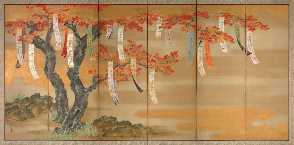Papers with Japanese text hang from a tree bearing red and gold leaves.